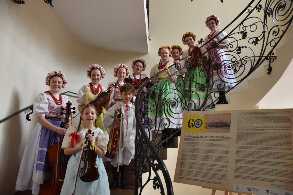 grupa dzieci w strojach ludowych i z instrumentami w rękach stoi na schodach