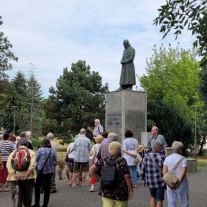 grupa ludzi wokół pomnika w formie postaci w długim płaszczu na cokole