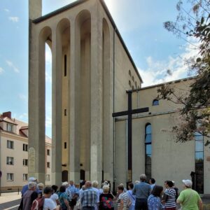 grupa osób przed wysokim nowoczesnym budynkiem z krzyżem na ścianie
