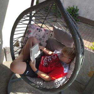 Młody chłopak leży i czyta książkę na fotelu wiszącym