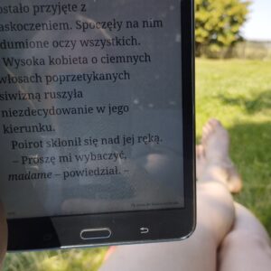 Czytnik ebooków, w tle fragment kobiecych nóg i ogród