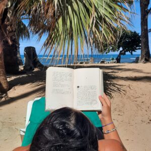 Kobieta leży na plaży wśród palm i czyta ksiązkę