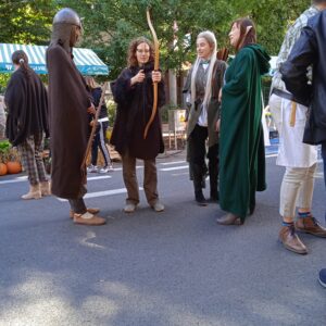 kilka osób stoi na ulicy, jedna trzyma łuk w rękach, pozostałe są przebrane za postaci z Hobbita