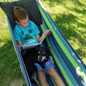Chłopiec leży na hamaku razem z psem i czyta książkę