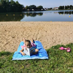 Dziewczynka czytająca książkę leży na plaży nad jeziorem