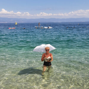 Kobieta z parasolką, trzyma książkę, w tle morze