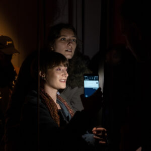 Dwie postacie patrzą na film fotograficzny. Postacie są oświetlone światłem latarki.