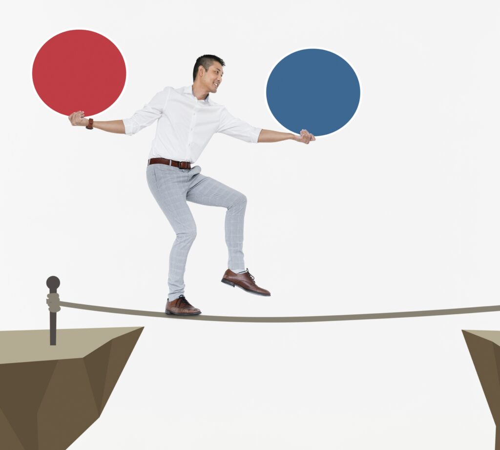 grafika przedstawia mężczyznę balansującego na linie, który w jednej ręce trzyma czerwone koło, a w drugiej niebieskie