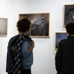 Dwie osoby oglądają zdjęcia w ramach powieszone na ścianach.
