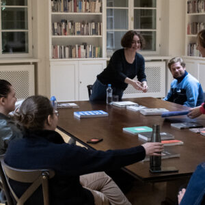 Olena Martynchuk stoi nad grupą osób zebranych w Filii Sztuki Biblioteki Raczyńskich i opowiada o książkach artystycznych, które jednocześnie pokazuje osobom uczestniczącym w spotkaniu.