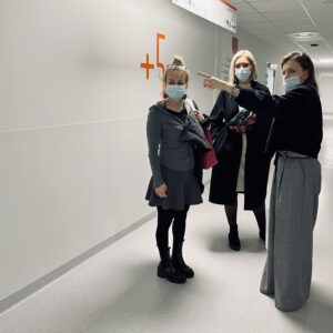 Na zdjęciu znajdują się trzy osoby rozmawiające na szpitalnym korytarzu.