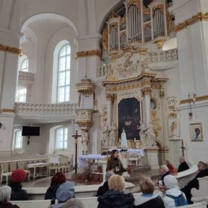 jasne wnętrze kościoła z widocznym ołtarzem, w ławkach siedzą ludzie