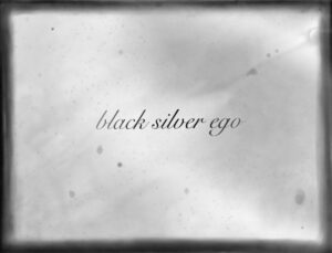 Grafika promująca wydarzenie. Czarno-białe tło. Na środku czarny napis: black silver ego.