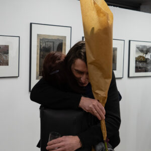 Dwie osoby przytulają się. Mężczyzna trzyma bukiet kwiatów.