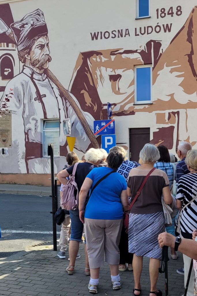 grupa ludzi patrzy na mural przedstawiający historyczną męską postać